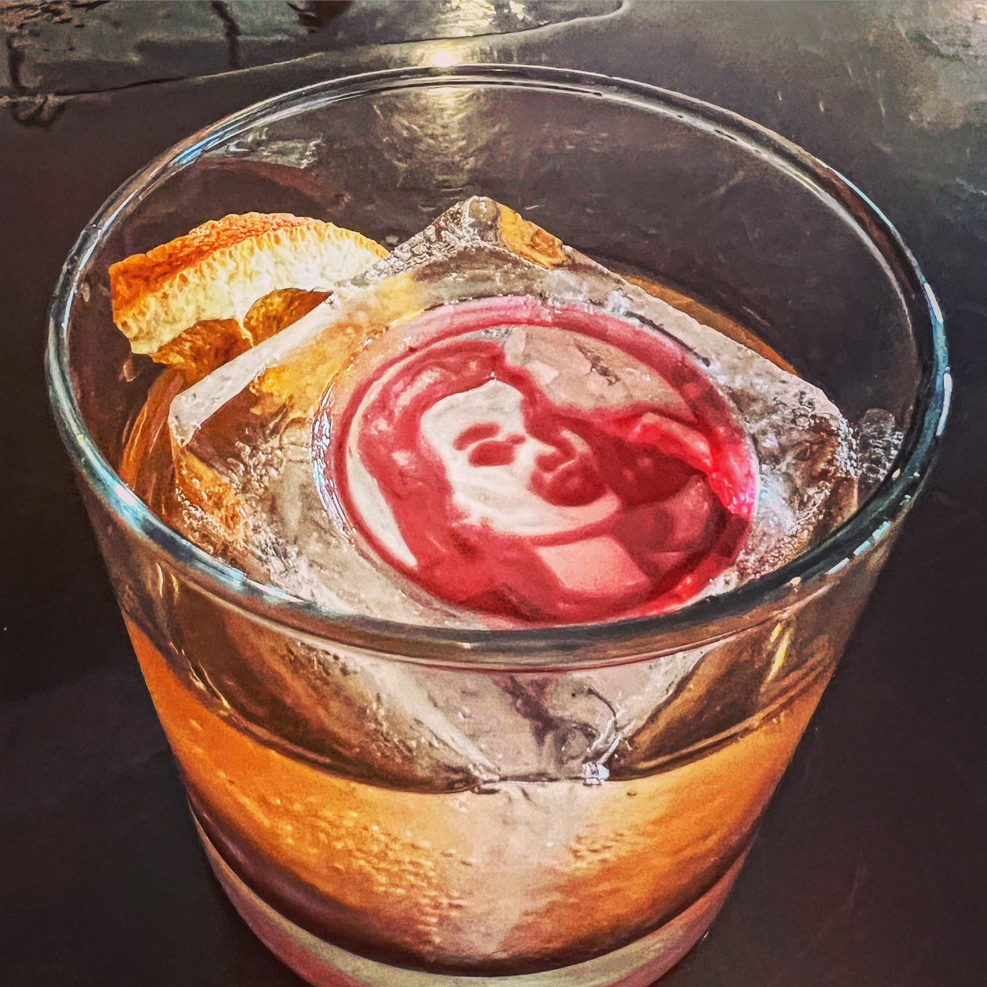 An old fashioned over clear ice stamped with the red Snitching Lady logo and a dried orange wheel