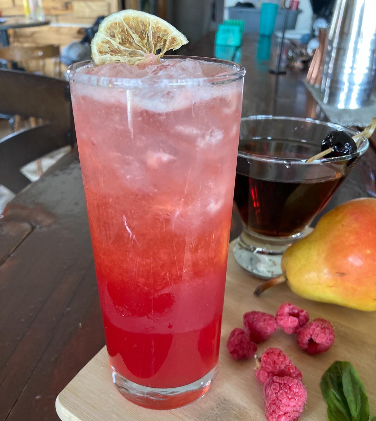 A tall raspberry Collins with a dried lemon wheel, pear and fresh raspberries
