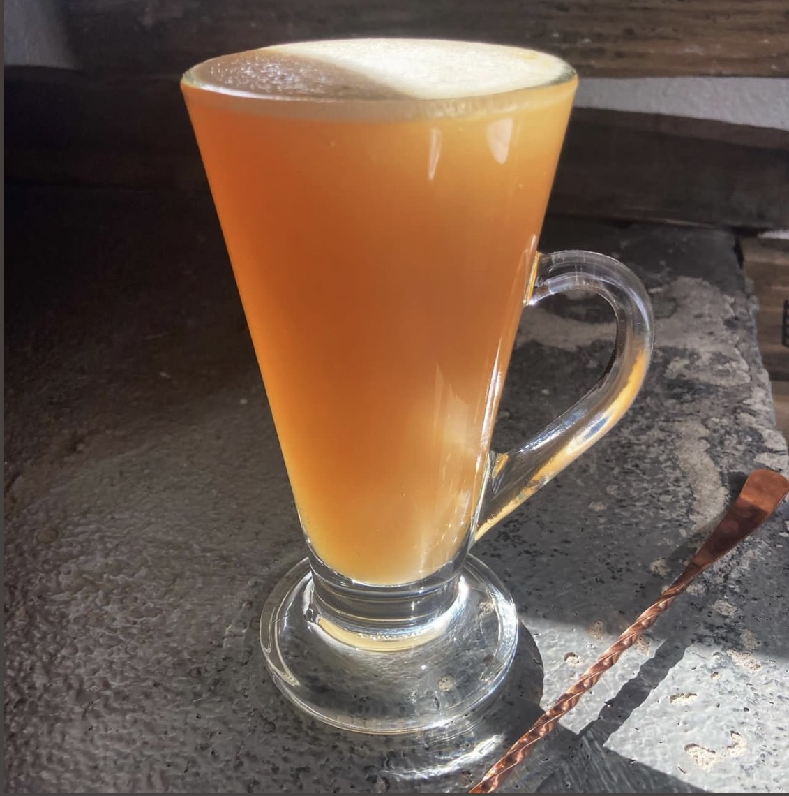 A hot buttered cider in a glass mug with a foamy top