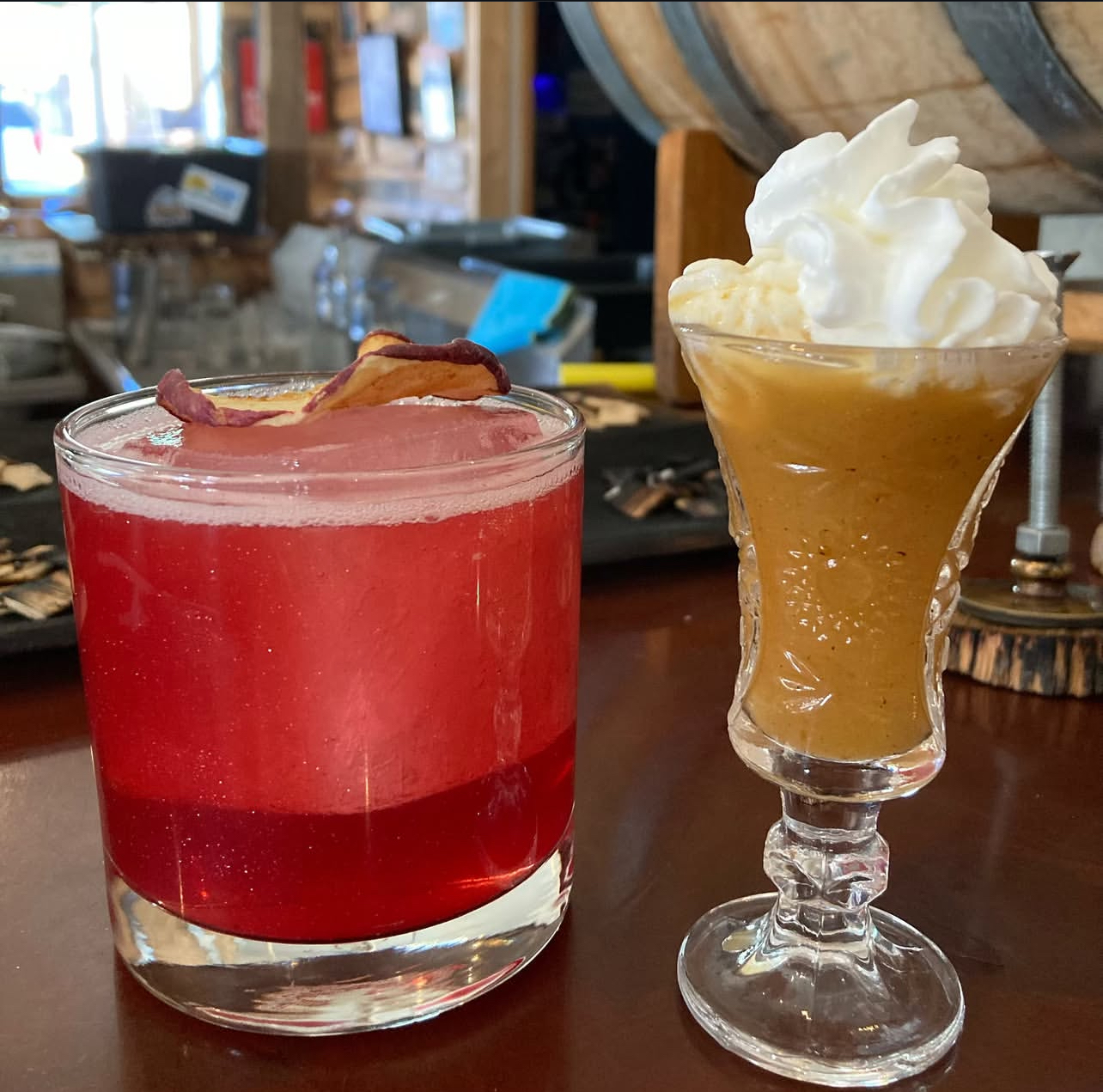 A crimson apple sour beside a whipped-cream-topped pumpkin cocktail in the still house