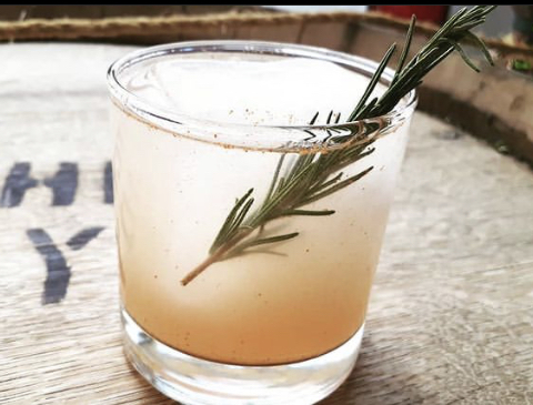 A spiced pear cocktail with a rosemary sprig on a barrel head