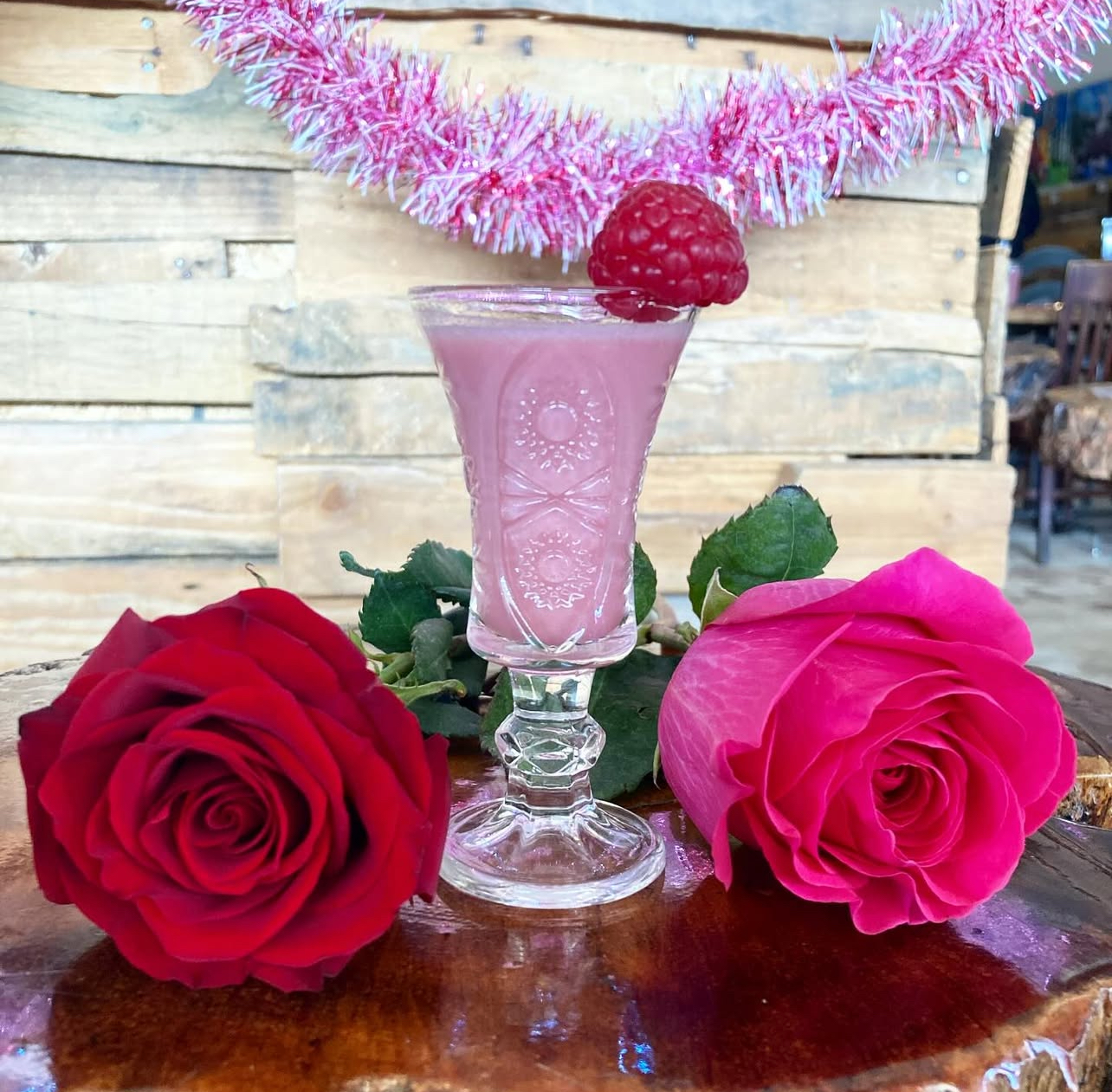 A rose-pink cordial in a vintage etched glass between two fresh roses