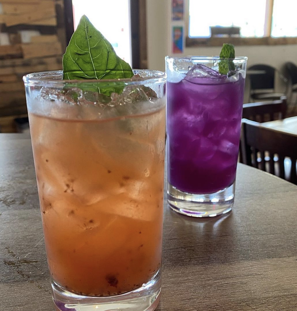 A strawberry basil smash beside a vivid purple shooter with mint