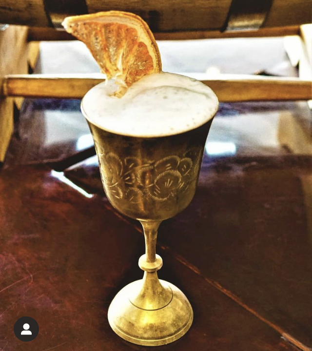 A frothy sour in an etched brass goblet topped with a dried orange wheel