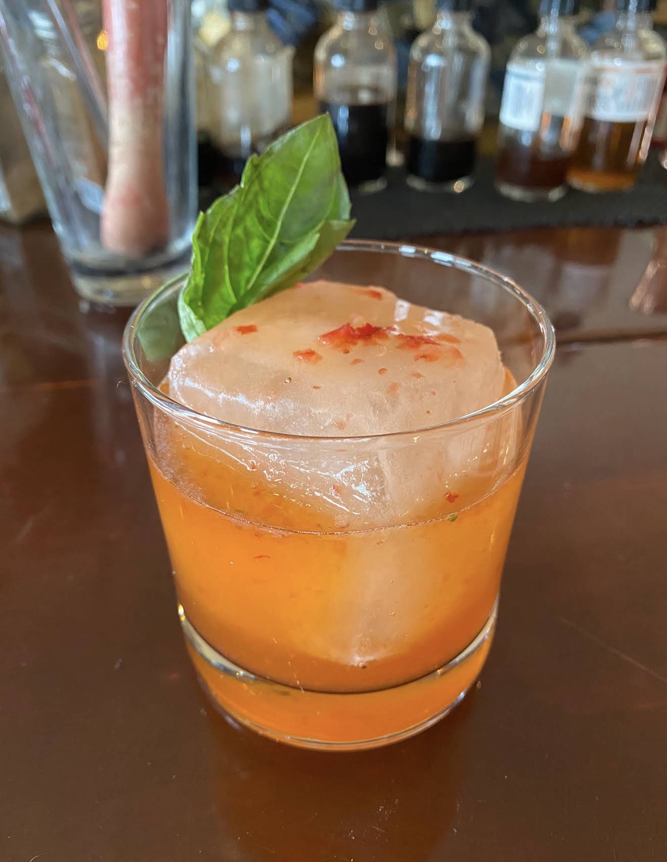 A strawberry basil old fashioned over a clear ice block