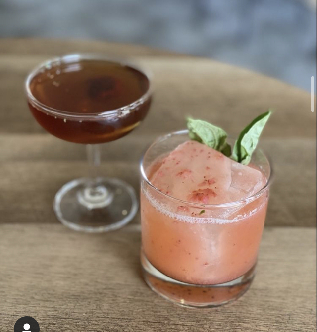 A Manhattan beside a strawberry basil smash on a wood table