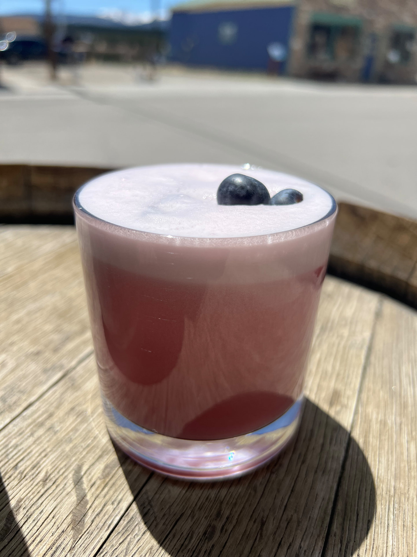 A blueberry sour with a foam cap and fresh blueberries in the sun