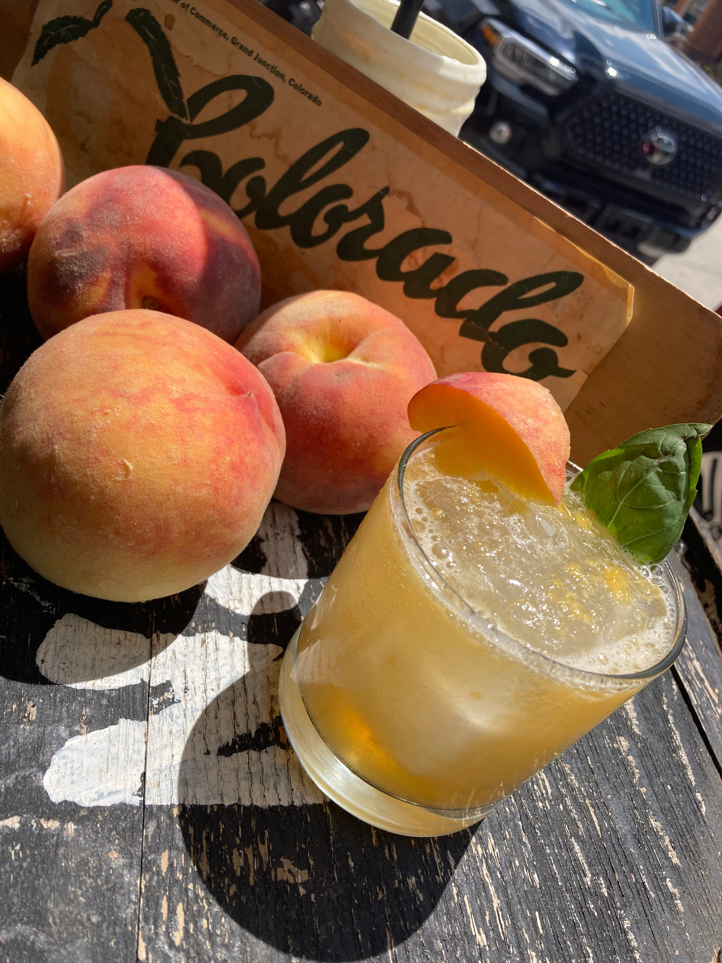 A Colorado peach and basil cooler beside a crate of fresh peaches