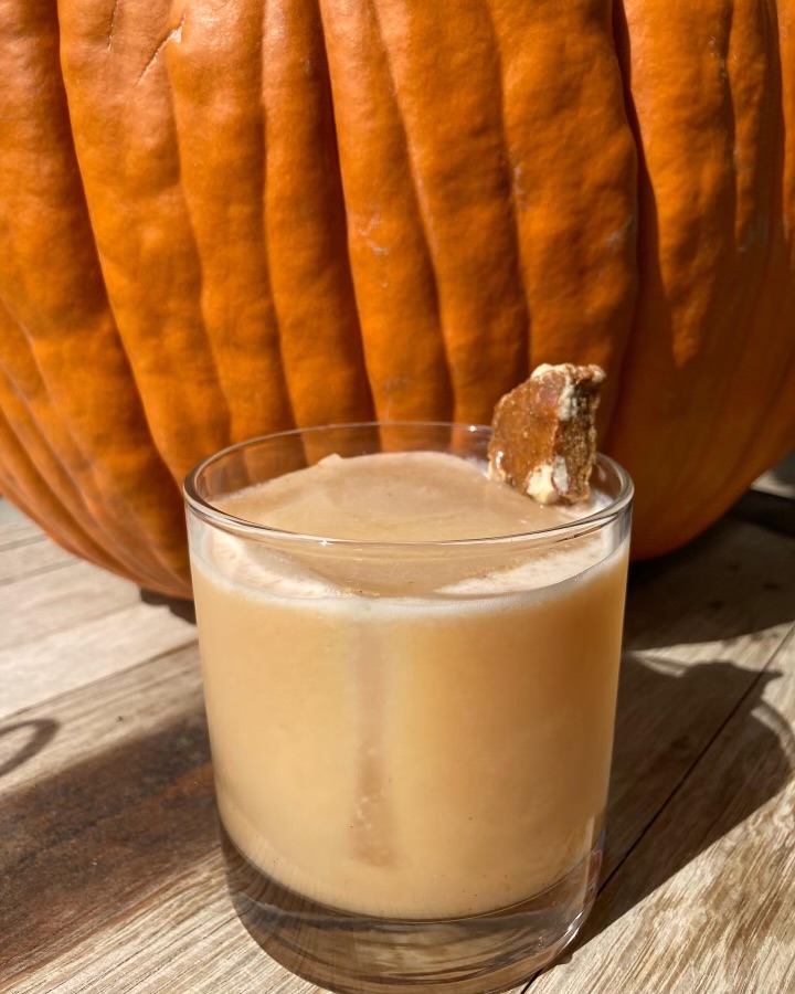 A pumpkin spice sour garnished with gingerbread beside a pumpkin