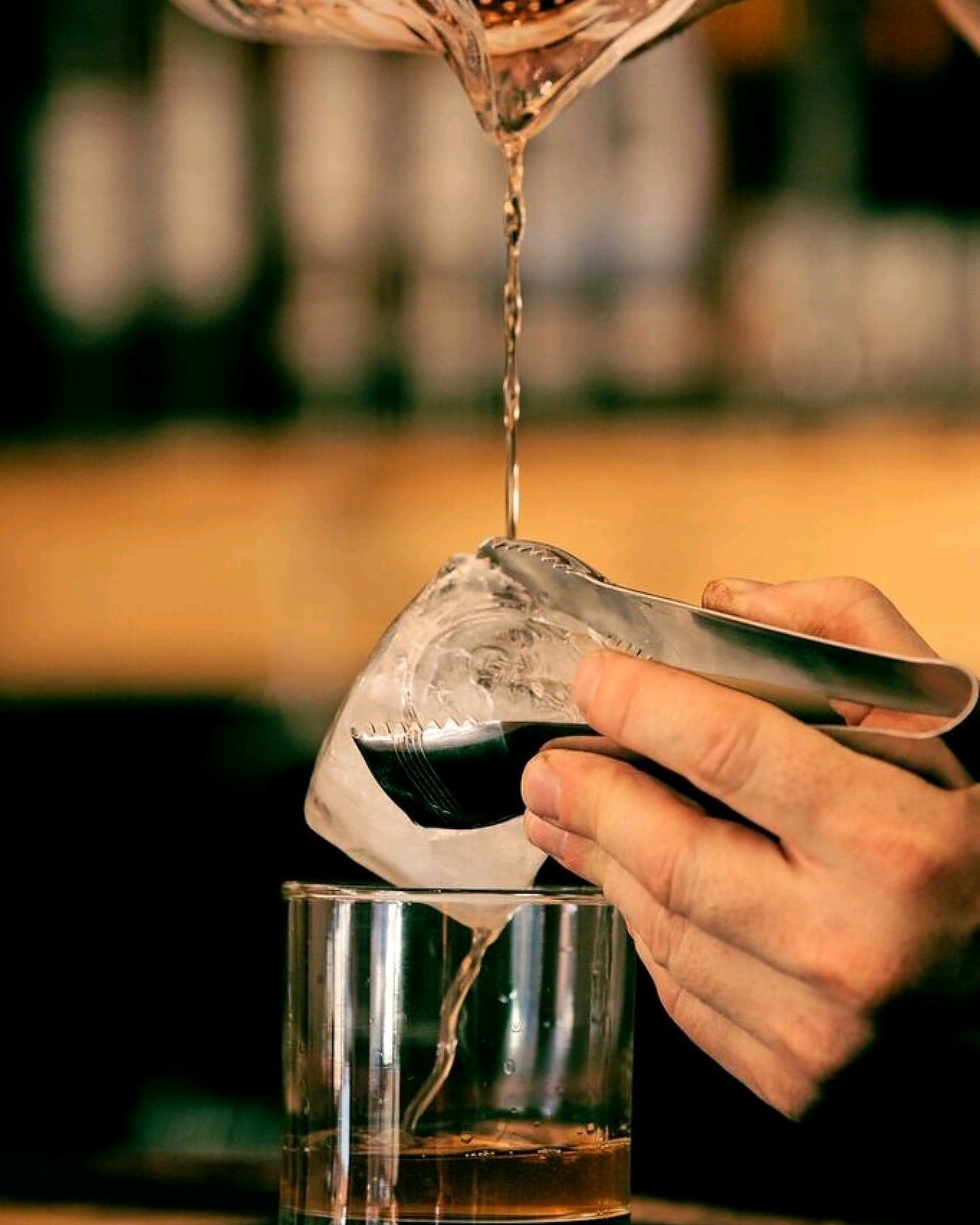 A bartender straining a stirred cocktail over a hand-cut ice cube