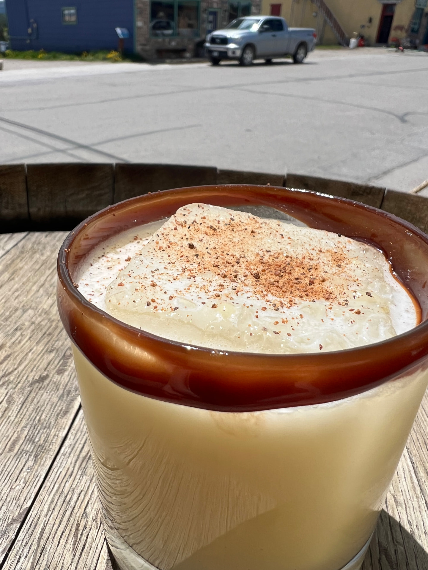 A caramel-drizzled cream cocktail dusted with nutmeg on a barrel table