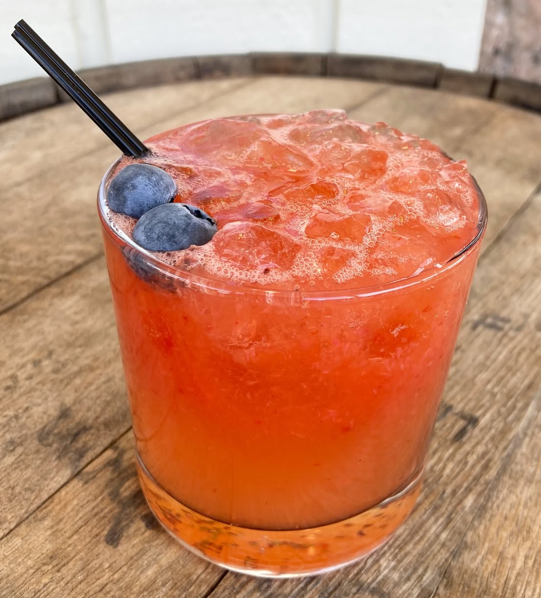 A crushed-ice berry smash topped with fresh blueberries on a whiskey barrel