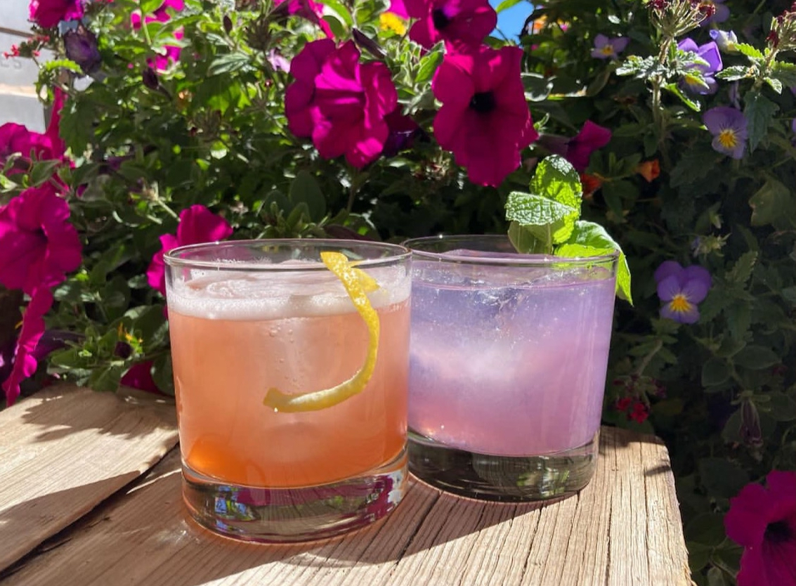 A blush sour and a lavender highball side by side among summer flowers