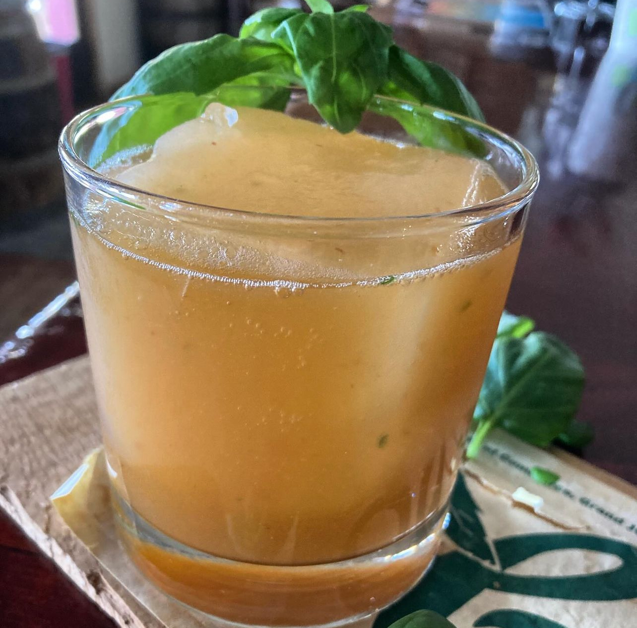 A peach and basil cocktail crowned with a fresh basil sprig