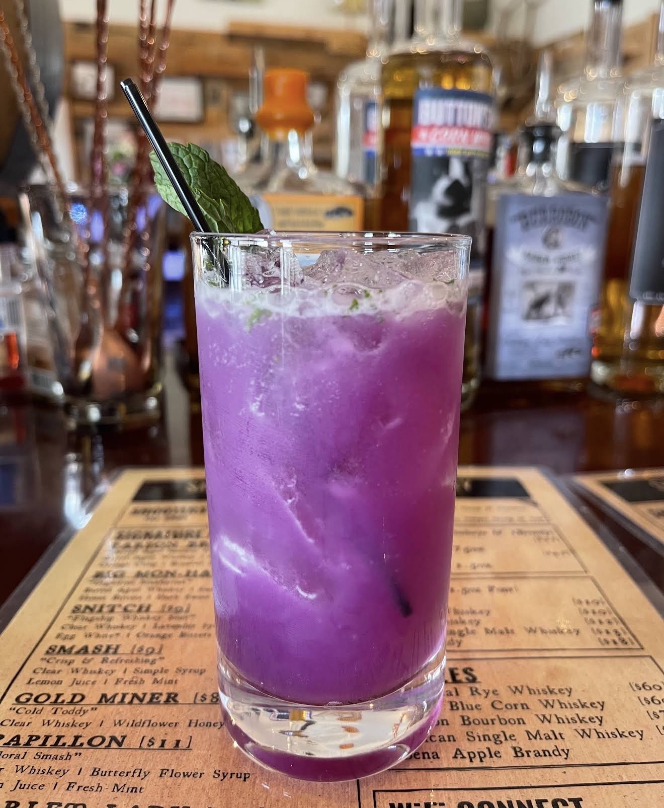 A vivid purple butterfly-flower smash with mint over the cocktail menu
