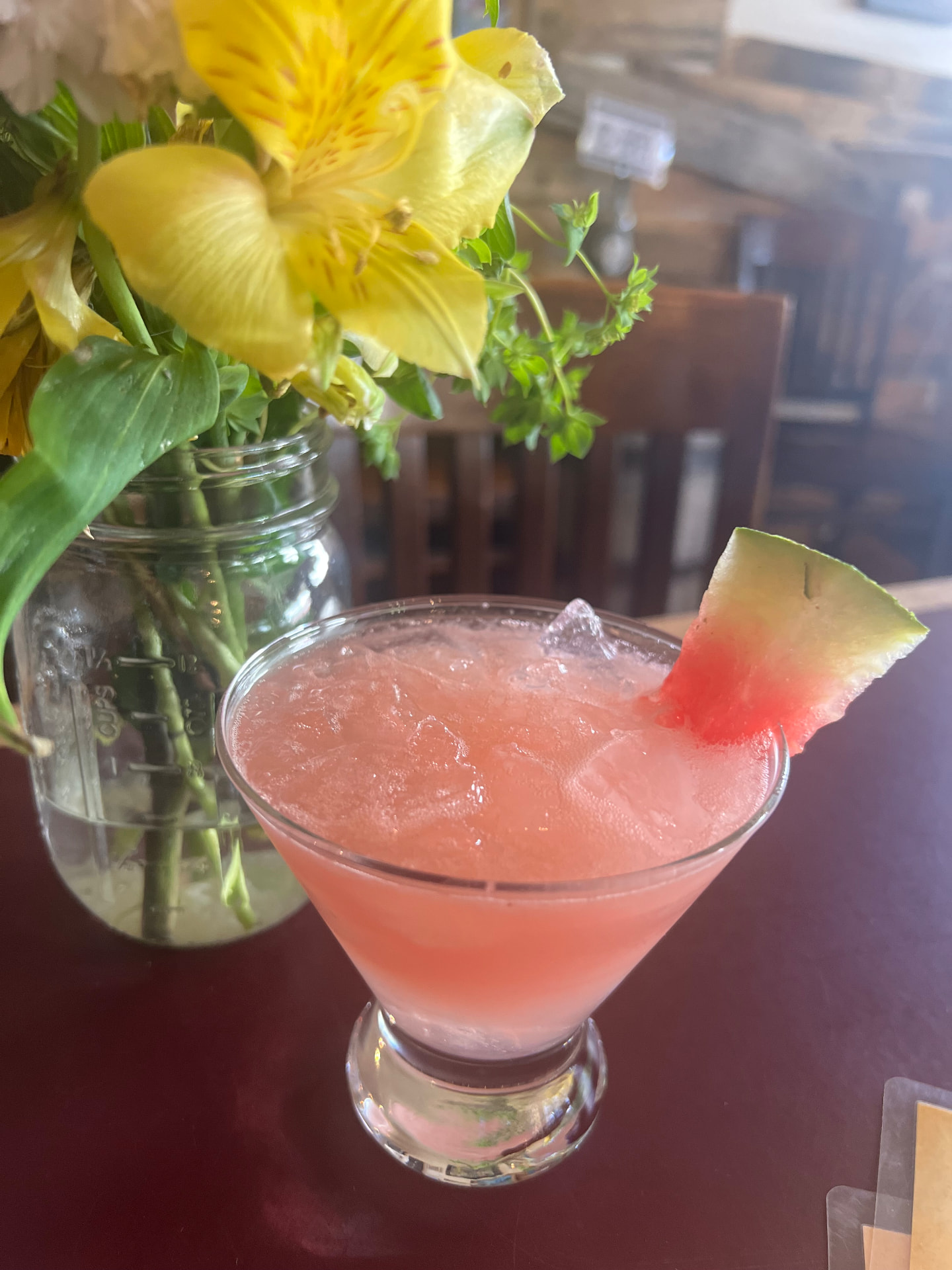 A watermelon martini with a fresh melon wedge beside garden flowers