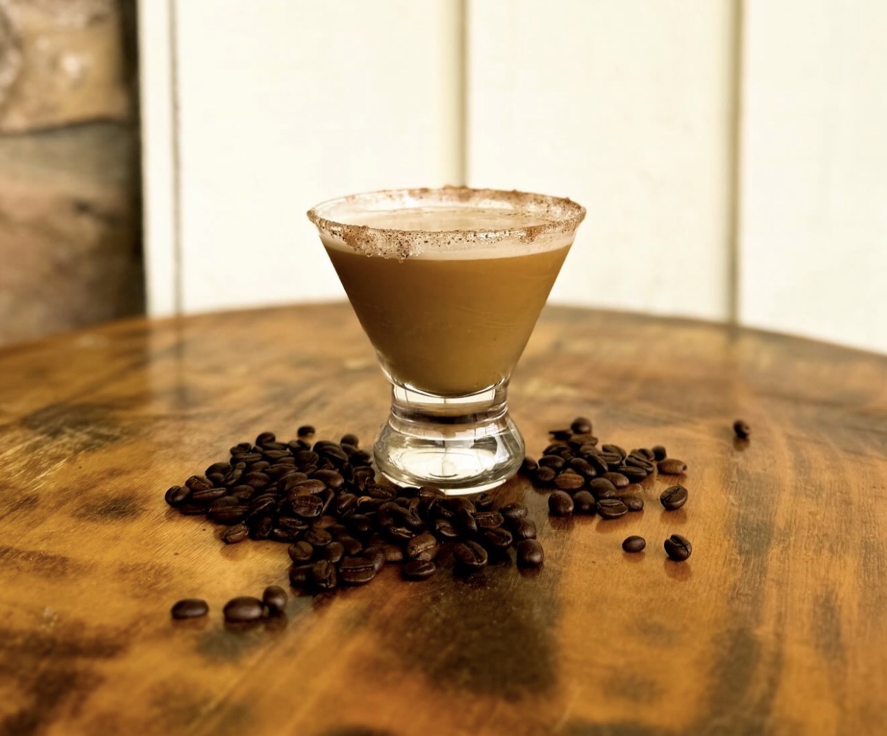 An espresso martini with a cocoa-dusted rim surrounded by roasted coffee beans