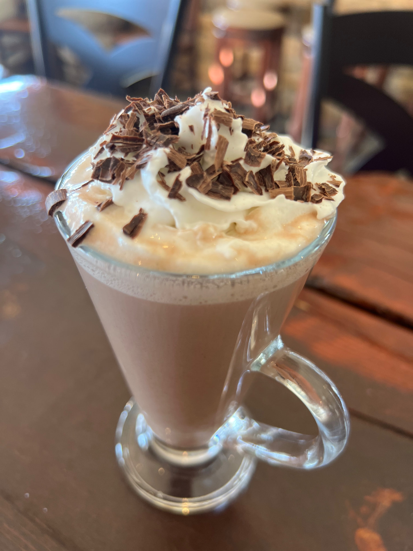 A spiked hot cocoa in a glass mug with whipped cream and chocolate shavings