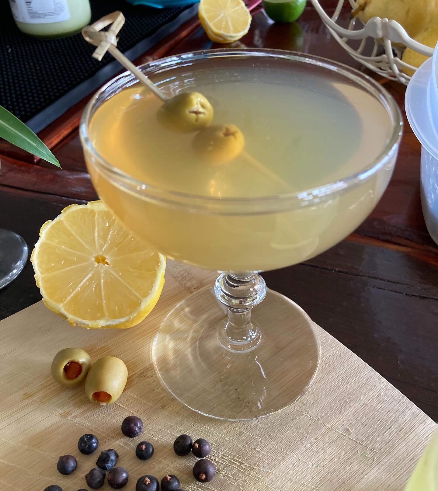 A dirty gin martini with olives, lemon and juniper berries on a bamboo board