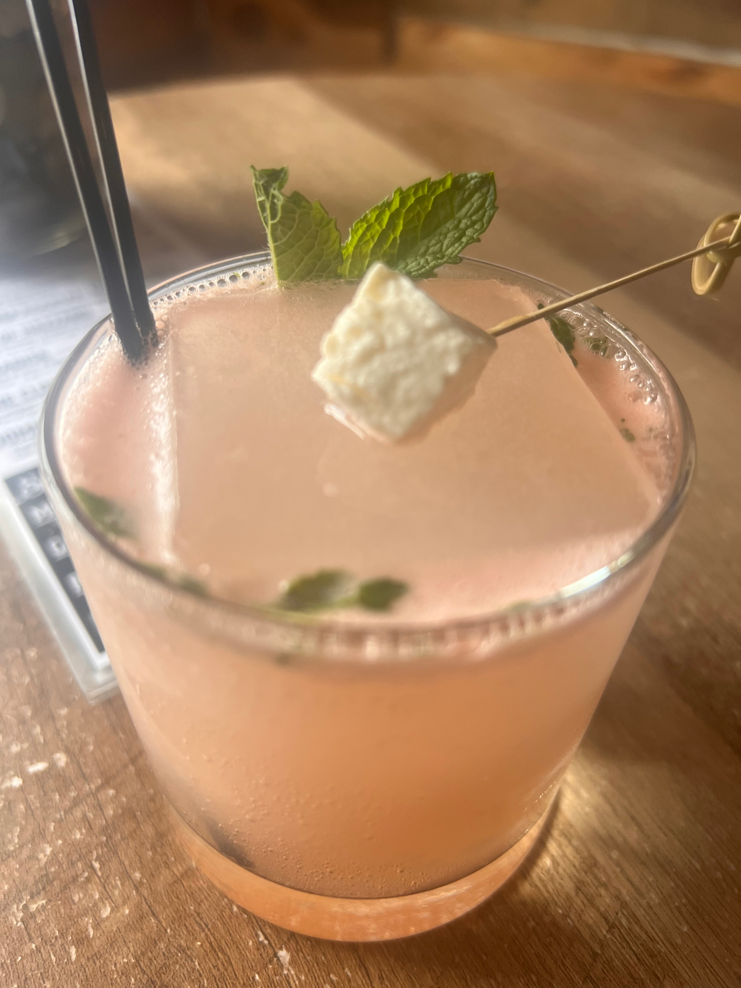 A pale pink cocktail with mint and a toasted marshmallow garnish