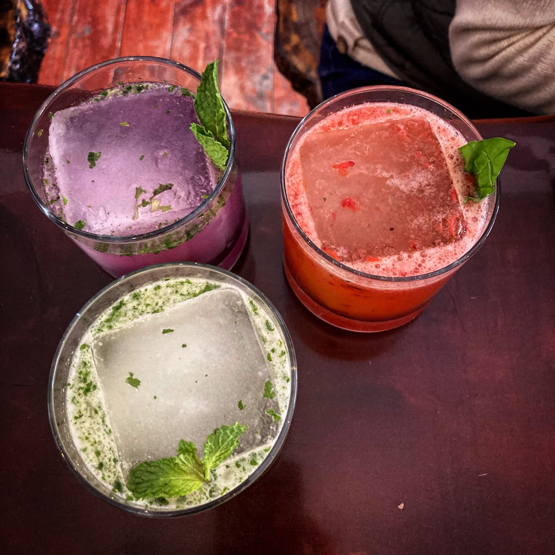 Three herb-topped cocktails over clear ice blocks on the bar top