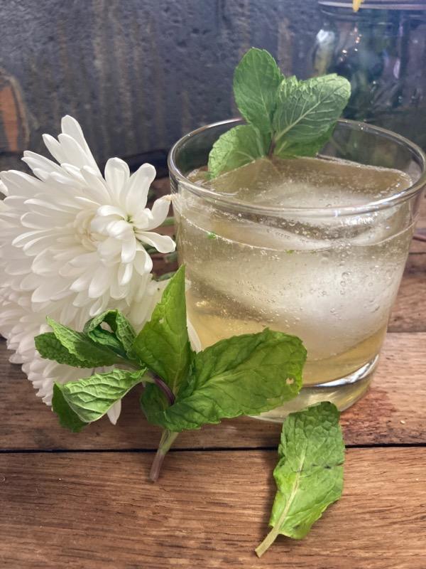 A sparkling mint highball beside a white chrysanthemum on weathered wood