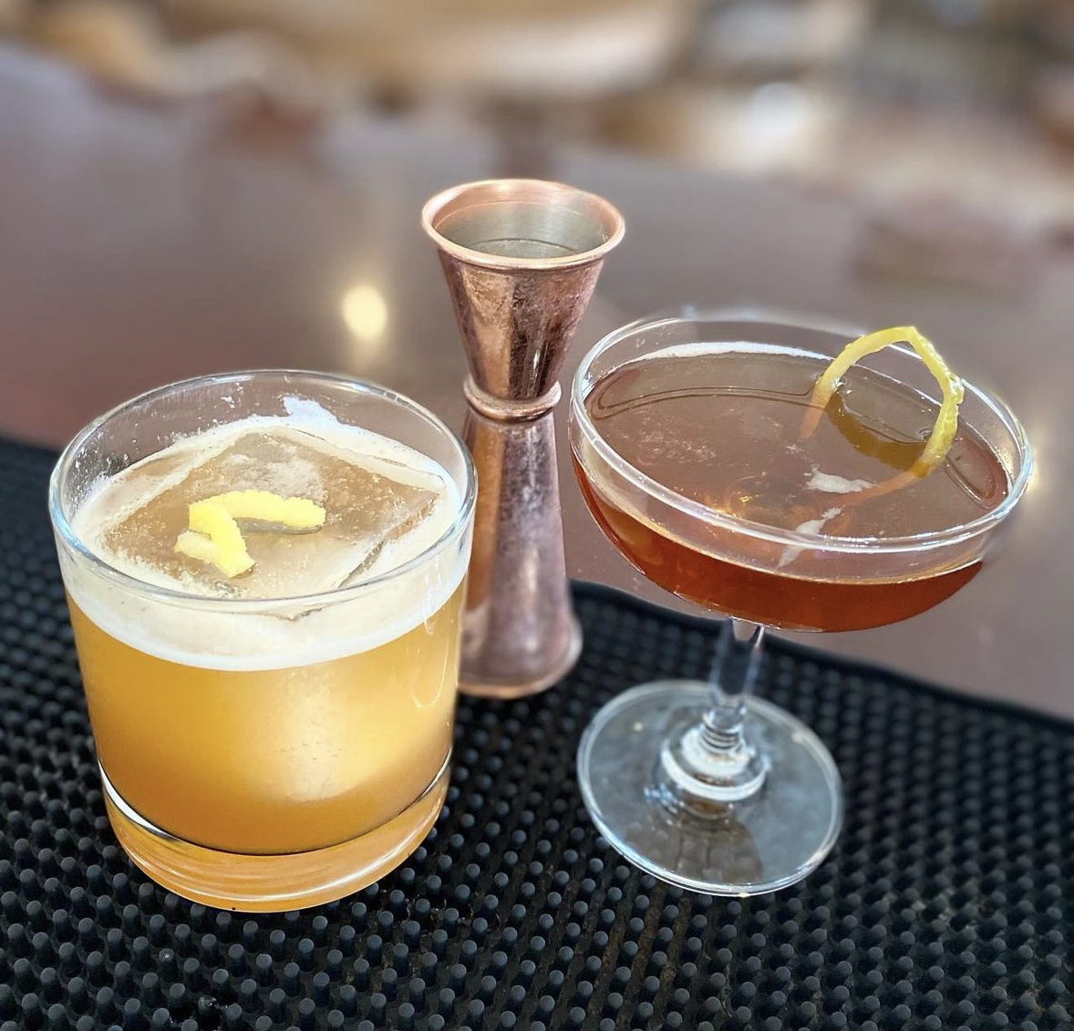 A whiskey sour and a Manhattan side by side with a copper jigger