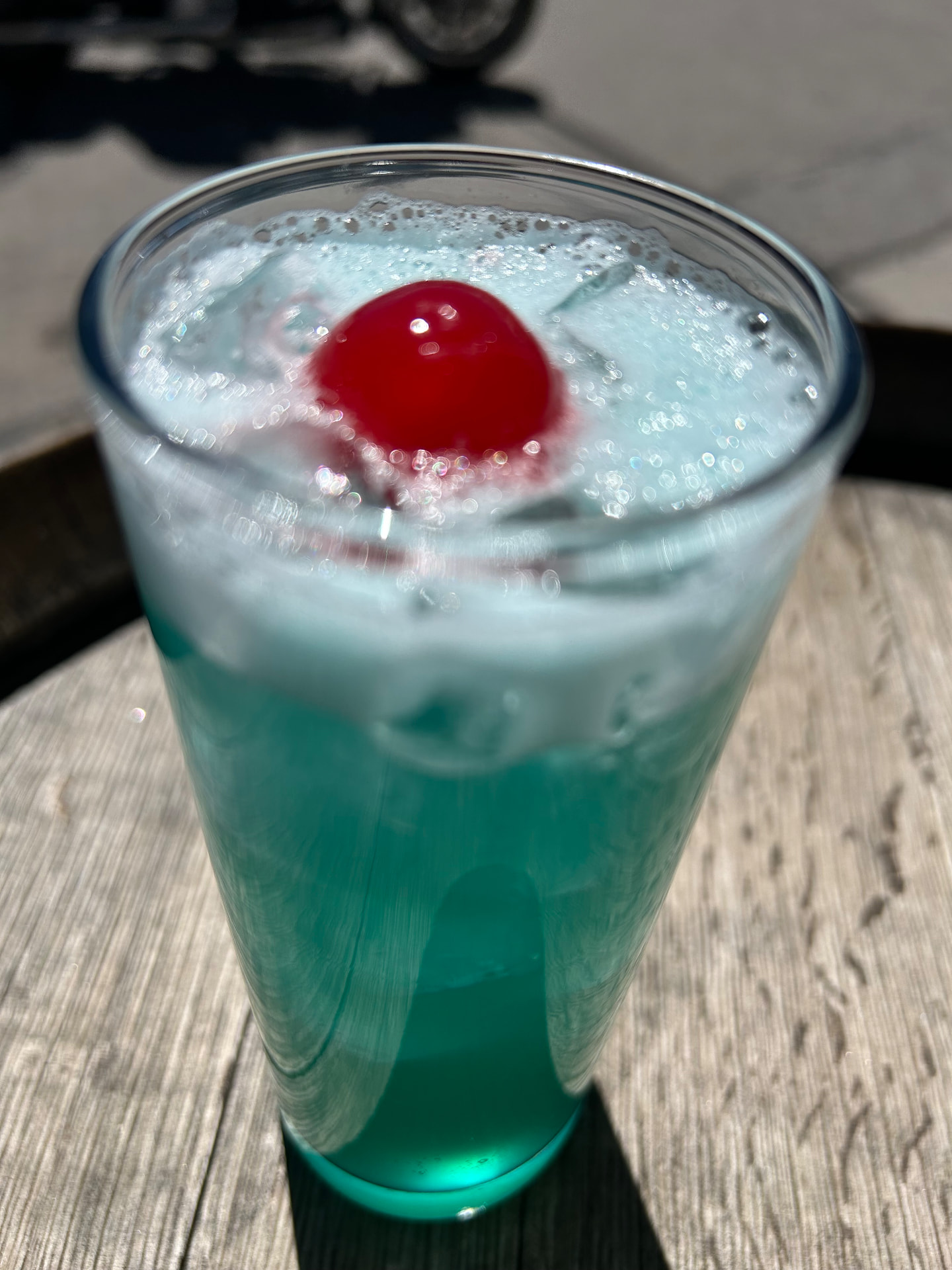 A frothy teal fizz topped with a bright cherry on the patio