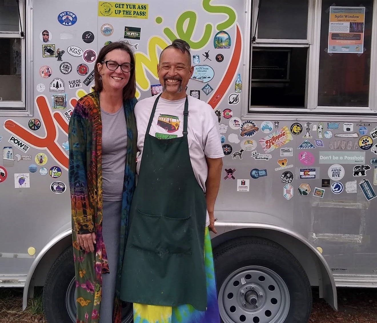The Yummies owners smiling in front of the sticker-covered food stand