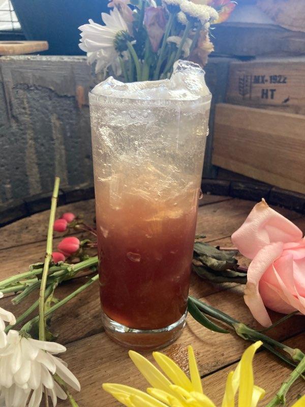 A layered berry highball with crushed ice among fresh flowers