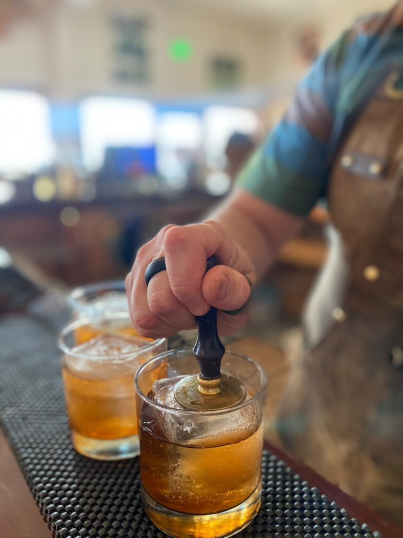 A bartender pressing a branded stamp into the clear ice of an old fashioned