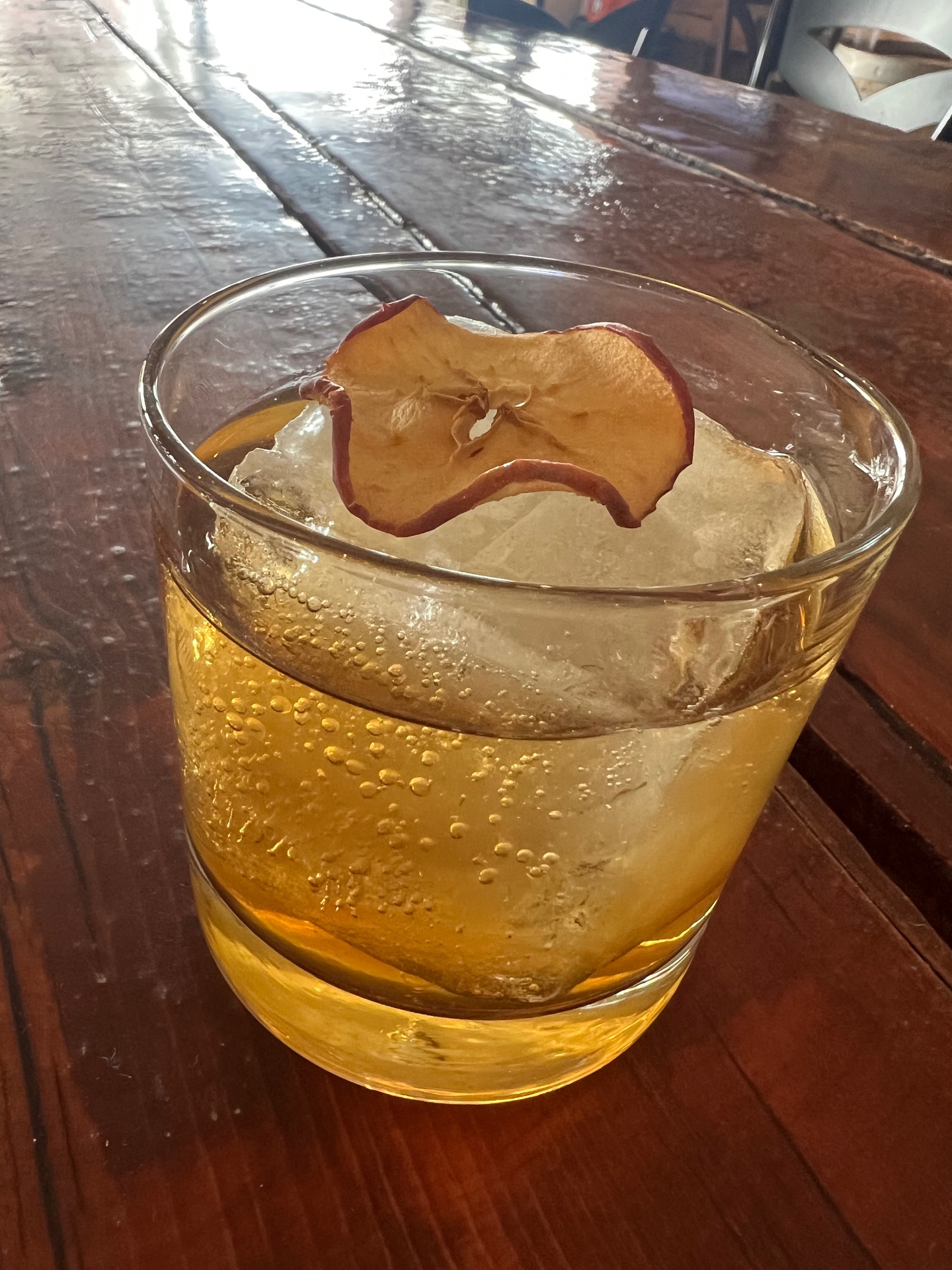 A sparkling apple highball over a hand-cut ice block with a dried apple wheel