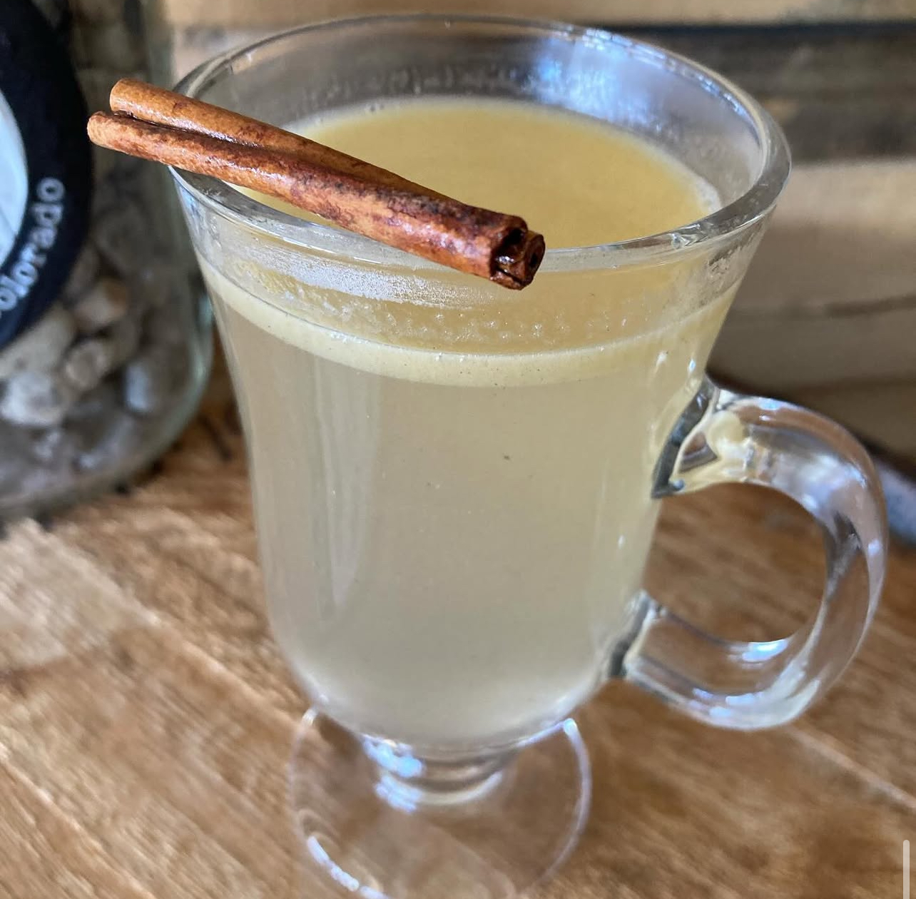 A hot buttered rum in a glass mug with a cinnamon stick