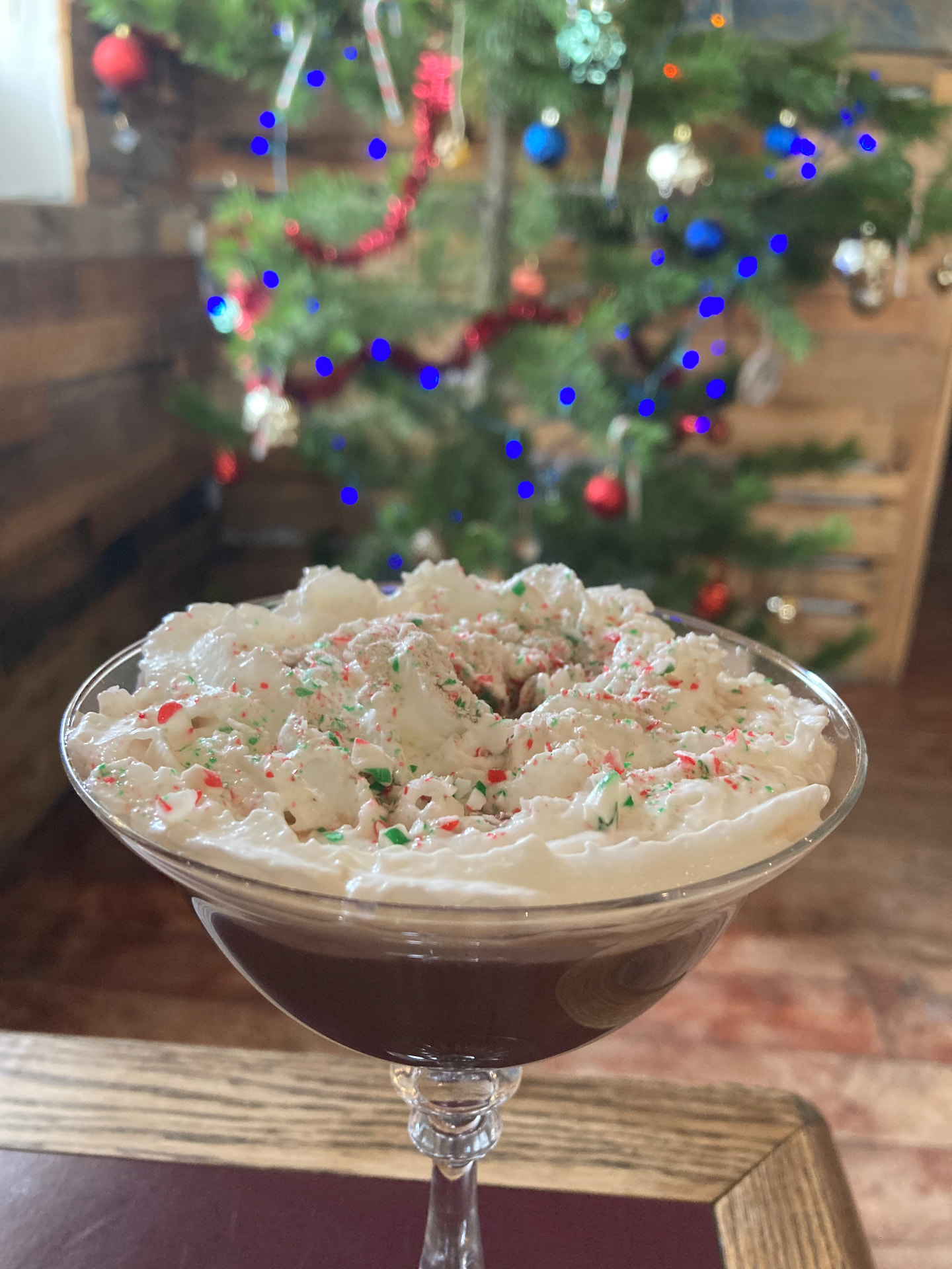 A chocolate peppermint martini piled with whipped cream and crushed candy cane by the Christmas tree