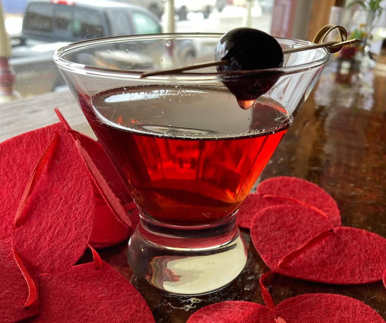 A cherry-topped Manhattan in a coupe glass among red felt hearts