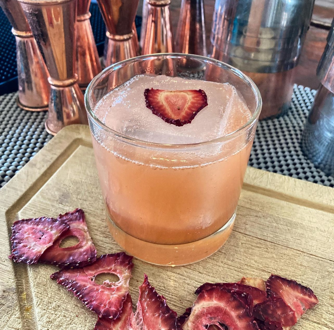 A strawberry sour over a clear ice block with dried strawberry chips