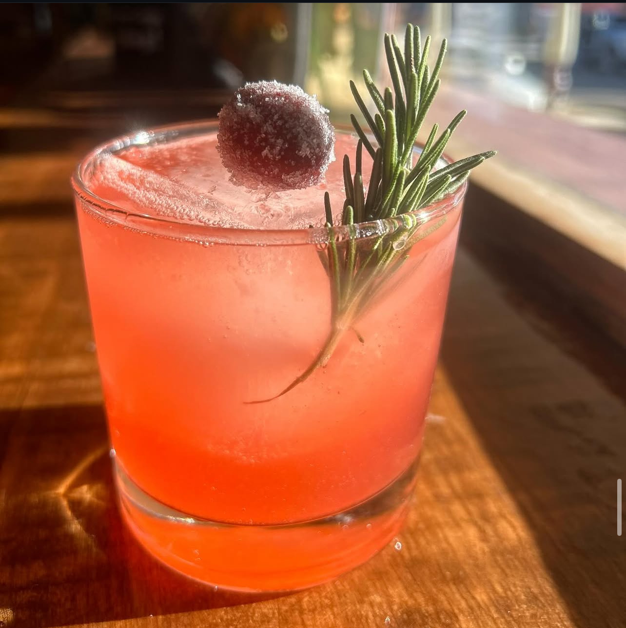 A sunlit cranberry cooler with a sugared cranberry and rosemary sprig