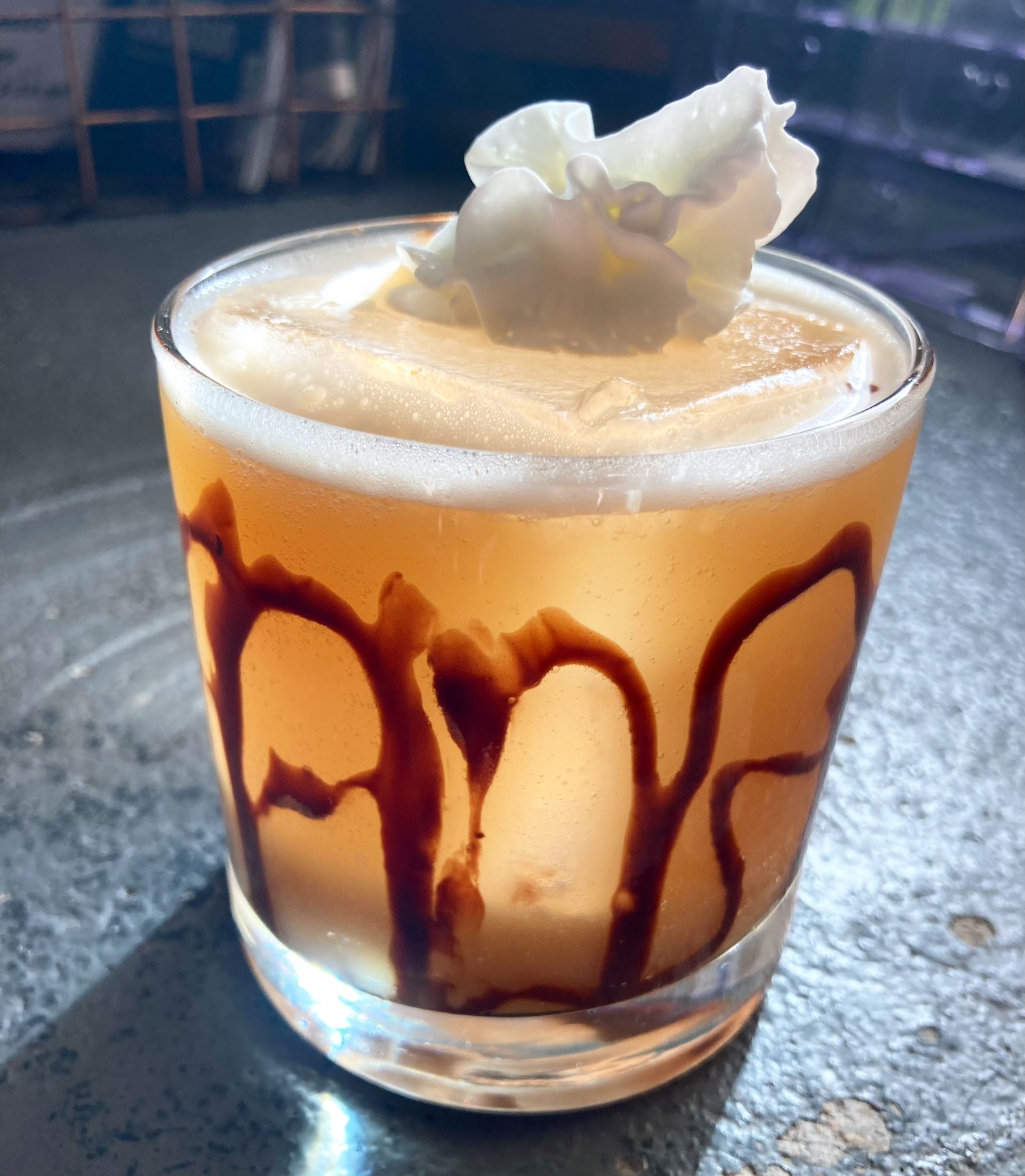 A frothy sour in a chocolate-drizzled glass topped with a white orchid