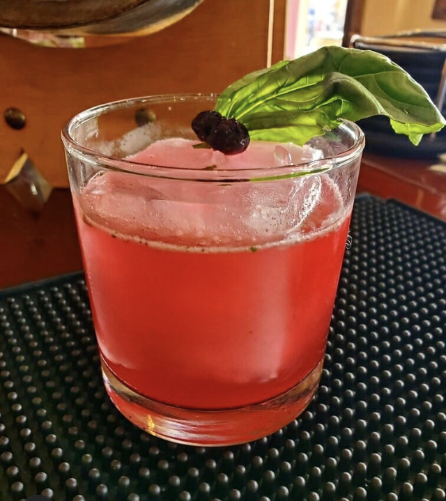 A ruby berry cocktail garnished with fresh basil and a brandied cherry