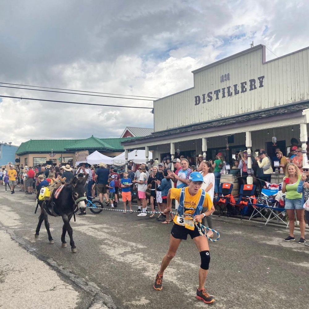 A pack-burro runner and a cheering crowd outside the distillery on Burro Days