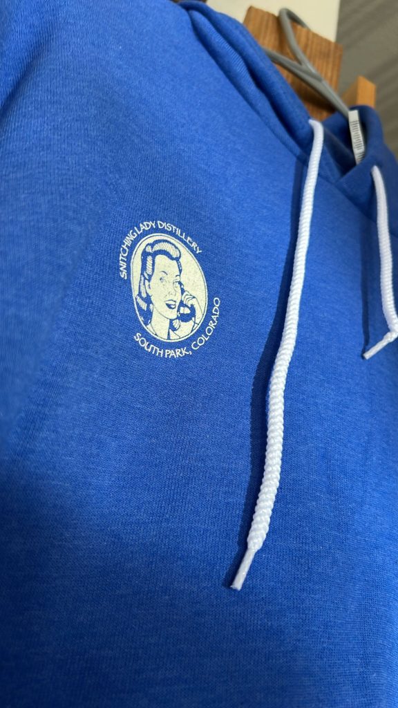 Royal-blue hoodie with the round Snitching Lady Distillery crest on the chest