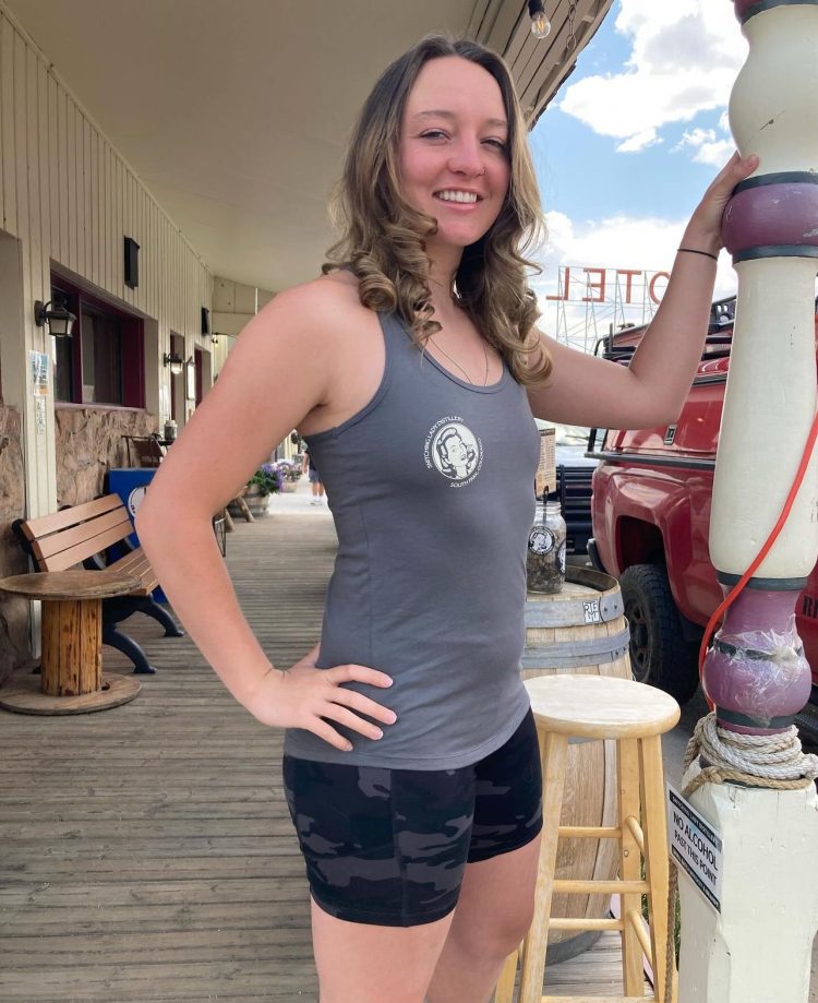 Gray racerback tank top with the round Snitching Lady crest, worn on the Front Street boardwalk