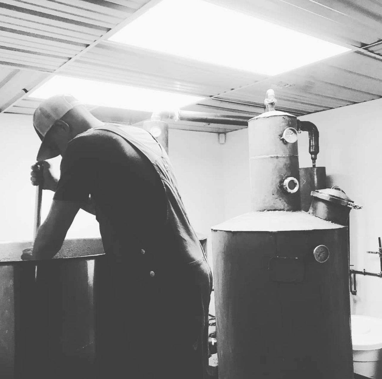 A Snitching Lady distiller working the mash beside the copper pot stills